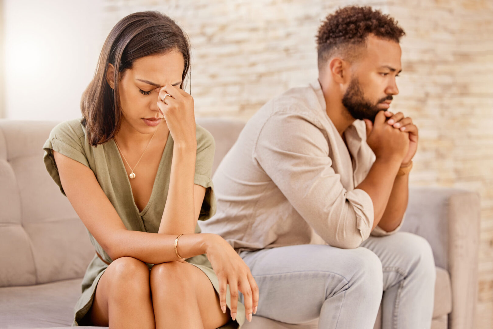 A woman and man sit on a couch, both appearing upset and deep in thought, facing forward with serious expressions.