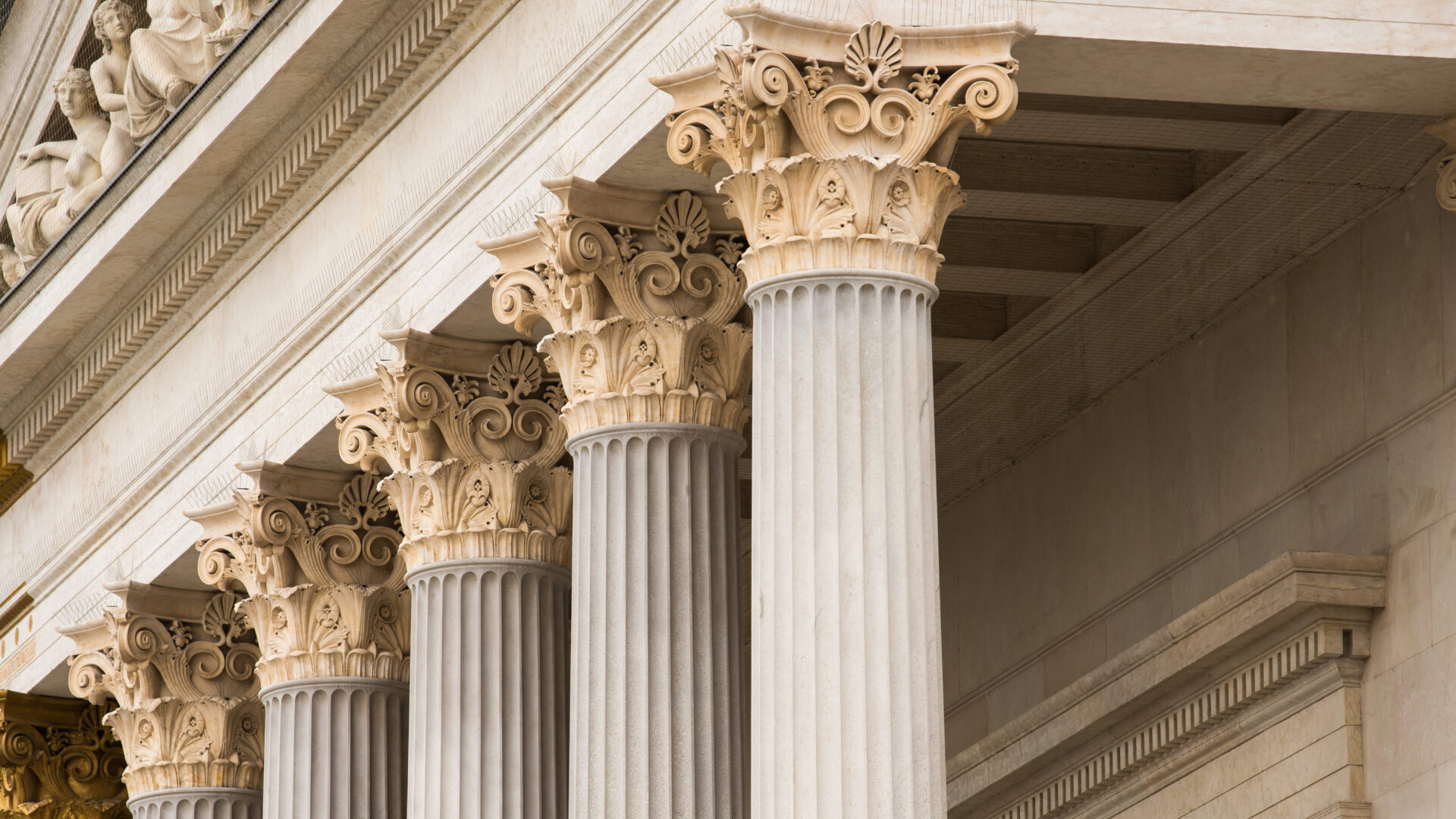 Close-up of a row of ornate Corinthian columns supporting an ancient Greek-style building with detailed carvings above.