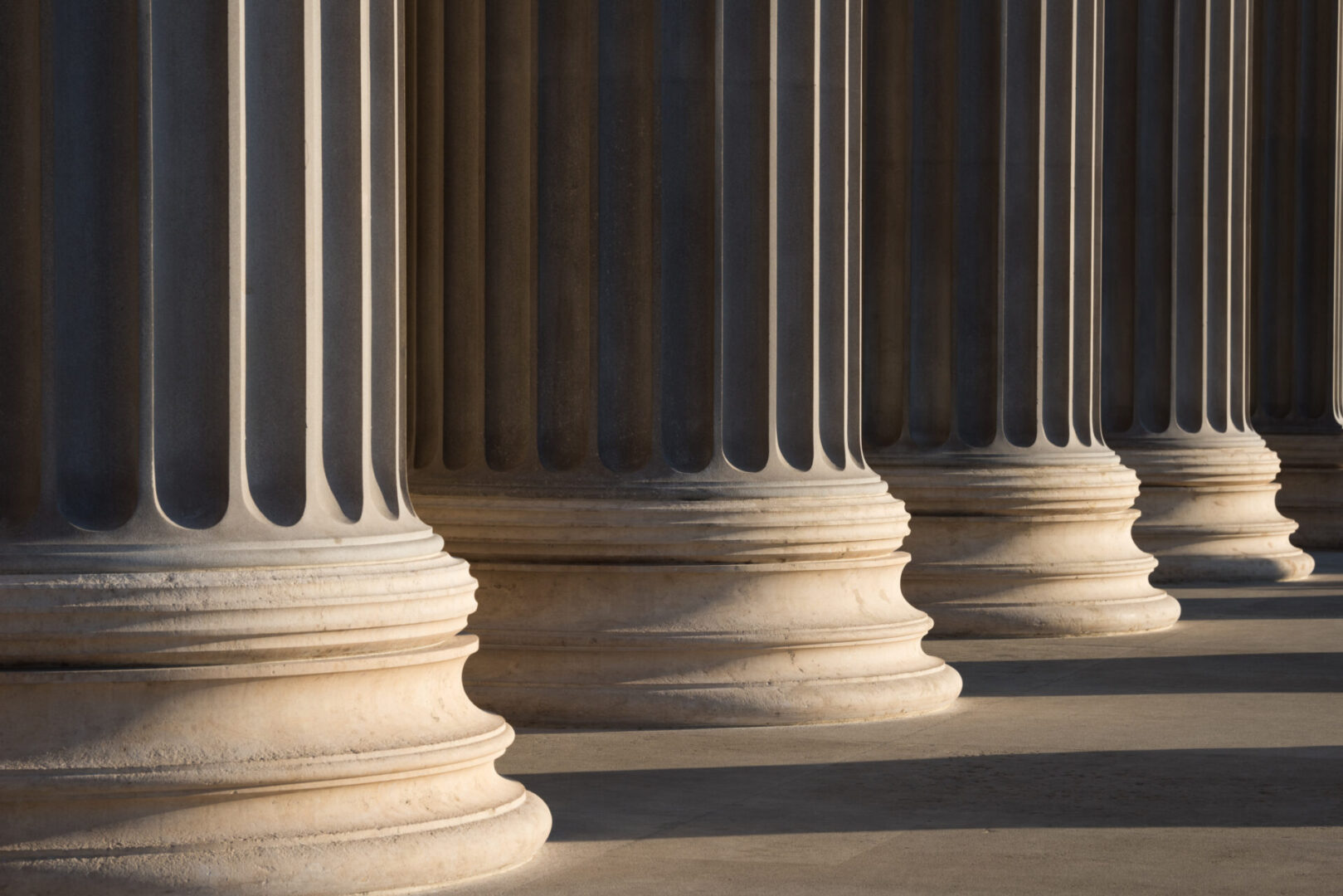 Row of tall, stone columns with intricate fluting, casting shadows on the ground.