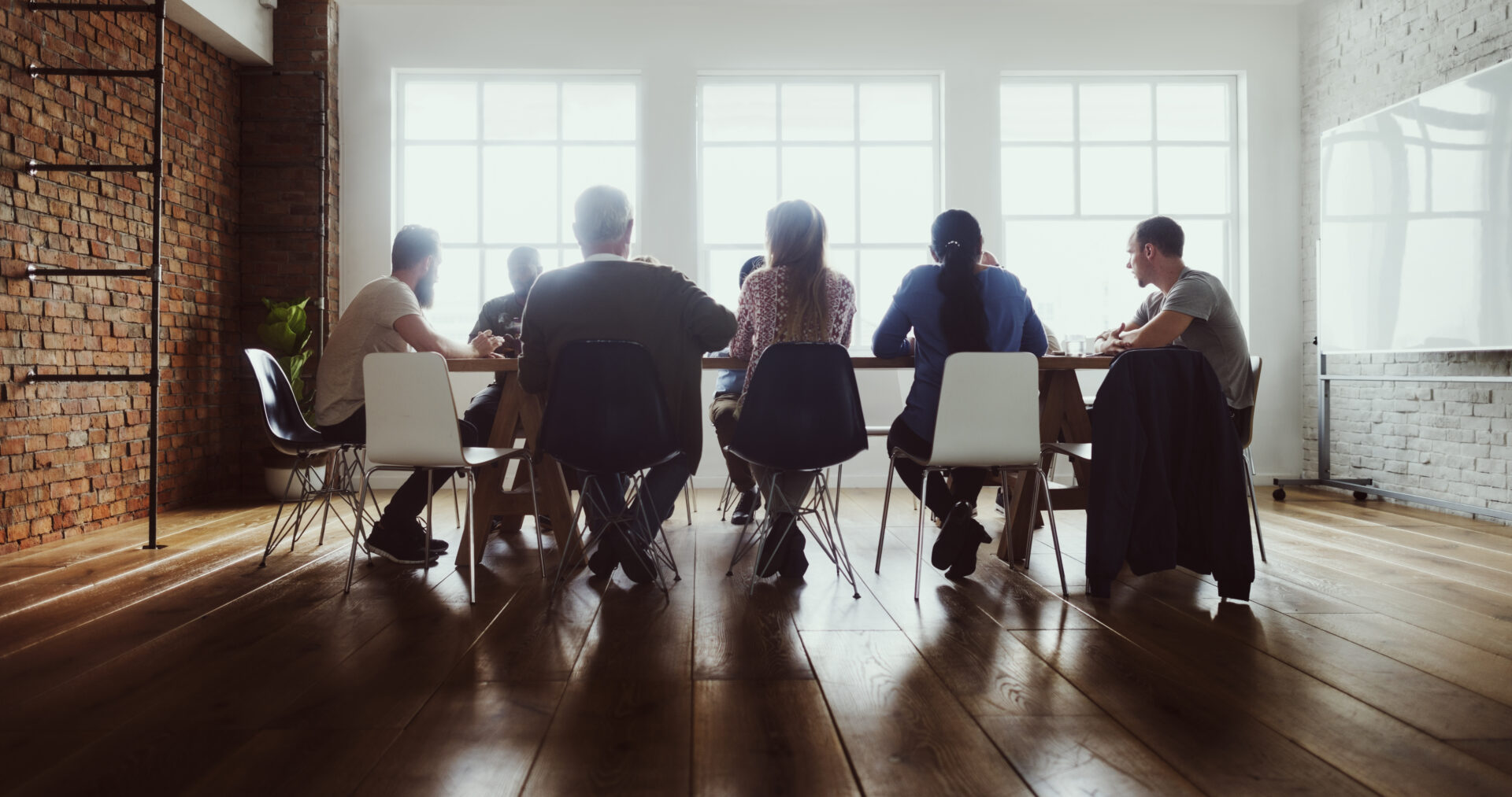 Seven people sitting at a conference table in a modern, well-lit meeting room with large windows.